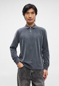 Γκρι πόλο μπλούζα με μακρύ μανίκι φτιαγμένη από μαλακό ύφασμα, με κλασικό γιακά, τρία κουμπιά και διακριτό κεντημένο λογότυπο στο στήθος.