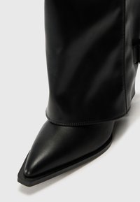 Bottine en cuir noir à bout pointu, texture lisse et détail de poignet distinctif. Présente des lignes épurées et des accents minimalistes.
