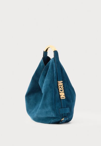 Sac à main en daim bleu avec poignée supérieure dorée et inscription dorée « MOSCHINO » sur la sangle latérale, présenté sur fond blanc.