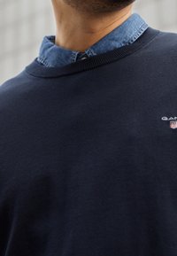 Granatowy sweter z okrągłym dekoltem, wykonany z bawełny. Posiada jasnoniebieski kołnierz z denimu i małe logo na klatce piersiowej.