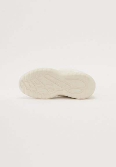 Semelle d'une basket en caoutchouc blanc cassé, avec un motif texturé et ondulé pour l'adhérence, un bout arrondi et des bords surélevés.