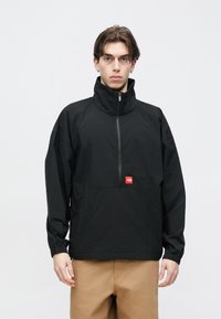 Μαύρο αδιάβροχο μπουφάν με ψηλό γιακά, μπροστινό φερμουάρ και κόκκινο έμβλημα. Διαθέτει ελαστικά μανσέτα και άνετη εφαρμογή. Ομαλή υφή υφάσματος.