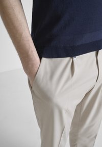 Suéter de punto azul marino con dobladillo acanalado, combinado con pantalones beiges de pinzas. Los pantalones tienen bolsillos laterales y un corte relajado.