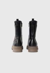 Bottines en cuir noir avec une surface texturée, fermeture éclair sur le côté et une semelle en caoutchouc épaisse beige. La vue arrière met en avant la hauteur et la silhouette.