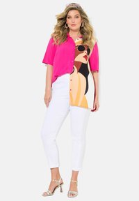 Chemise rose vif à manches courtes avec détails de boutons, présentant une impression de portrait ; associée à un pantalon blanc slim et des sandales à talons argentées.