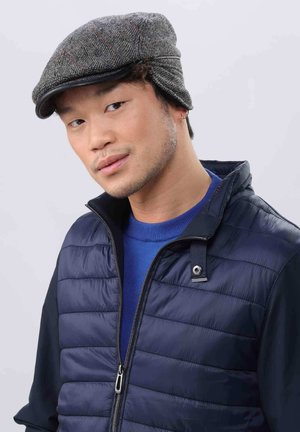 Gray tweed flat cap with a hounds-tooth pattern and subtle red accents, paired with a navy quilted vest and a blue sweater underneath.