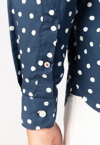 Camicia in cotone blu navy con pois bianchi. Caratterizzata da un polsino arrotondato con chiusura a bottone e un colore del bottone a contrasto. Tessuto morbido.