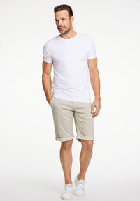T-shirt bianca a maniche corte abbinata a pantaloni beige arrotolati e sneakers bianche. Abbigliamento casual e comodo con un design semplice.