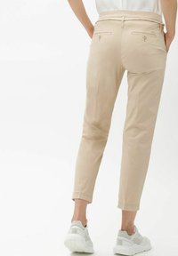 Pantalons beiges fuselés avec une texture lisse, dotés d'une ceinture en corde, de poches arrière et d'une longueur raccourcie, associés à des baskets blanches.