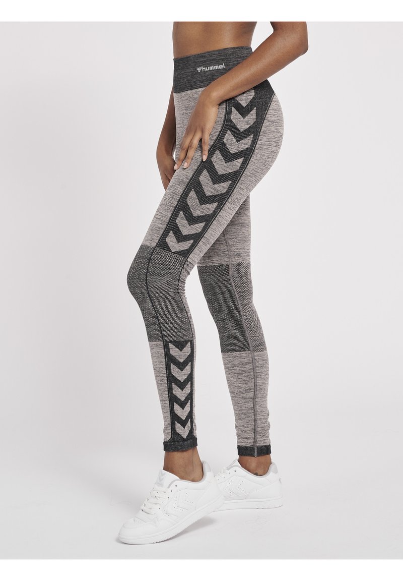 Svarta och grå högmidjade leggings med ett chevronmönster längs sidan, tillverkade av ett strukturerat, elastiskt tyg. Vita träningsskor bärs.