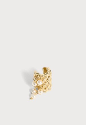 Gold strukturierter Ohrreif mit kleinen hängenden weißen Perlen auf schlichtem hellgrauem Hintergrund.