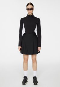 Czarna bluzka z długim rękawem z białymi panelami bocznymi i suwakiem na ćwierć. Czarna plisowana spódnica. Czarne sneakersy i białe skarpetki typu crew dopełniają strój.