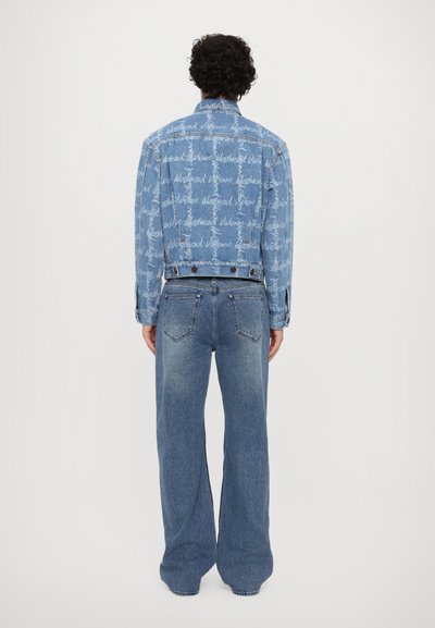 Denim jacket featuring a light blue wash with white script design, paired with matching flared jeans. Both garments have a relaxed fit.