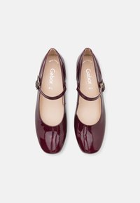 Bordowe lakierowane buty Mary Jane z okrągłym noskiem, pojedynczym paskiem i regulowanym klamrą; gładka faktura i minimalistyczny design.