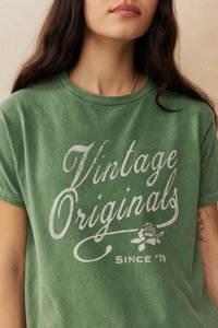 Žalias medvilninis marškinėliai su vintage stiliaus baltu grafiku: "Vintage Originals" ir rožės dizainu su "Since '79" apačioje.