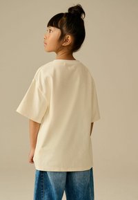 Crème-kleurige oversized katoenen t-shirt met korte mouwen, ronde halslijn en een ontspannen pasvorm, gecombineerd met denim broek. Eenvoudig, effen ontwerp.
