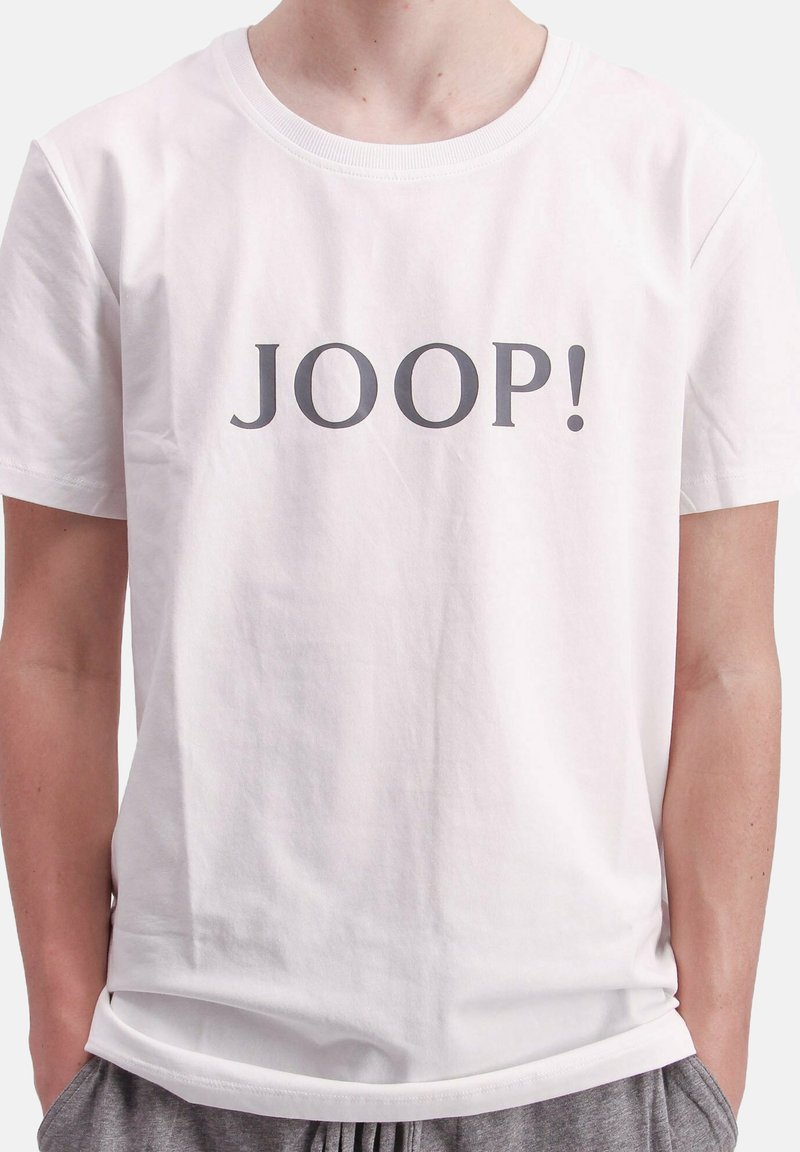 Witte katoenen t-shirt met korte mouwen, met in het midden op de voorkant de tekst "JOOP!" in een vet grijs lettertype. Eenvoudig en klassiek ontwerp.