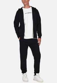 Black zip-up hoodie, white crew neck t-shirt with "LES CLASSIQUES" print, black jogger pants, and white sneakers on a plain background.