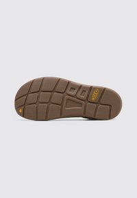 Suela de zapato de goma marrón con un patrón de tracción que presenta acentos rectangulares y hexagonales, etiquetada "CONTUR ARCH" y un logo de triángulo amarillo.