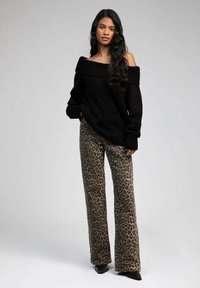 Pull noir à épaules dénudées avec des bords côtelés, associé à un pantalon large en imprimé léopard beige et marron foncé. Talons aiguilles noirs.