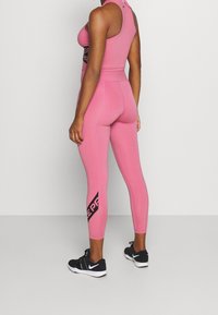 Sostén deportivo rosa y leggings a juego hechos de material elástico, con marcado negro en el costado y un diseño ajustado.