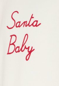 Witte stof met rode borduursel dat "Santa Baby" in cursieve letters spelt. Het ontwerp heeft een zachte textuur en een sterke tegenstelling tussen de kleuren.