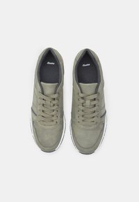 Žalios zomšos sportbačiai su apvaliu nosiu, tekstūruotomis raištelėmis, pilkais akcentais ir balta guma. Ženklo vidpadis su kasdiene dizaino estetika.