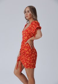 Röd klänning med orange blommönster, kort ruched-design, puffärmar och sidodragband. Slät tyg med figursydd silhuett.