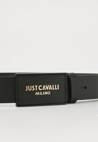 Svart belte laget av glatt lær med en rektangulær spenne med gyldne bokstaver "JUST CAVALLI MILANO." Minimalistisk design, ingen synlige mønstre.