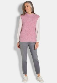 Rosa gerippter Pullover mit grauem Langarm-Unterlayer, kombiniert mit grauen taillierten Hosen und weißen Sneakers. Schlichtes und lässiges Design.