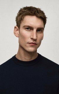 Mornarski pleteni pulover s visokim okruglim izrezom, ističe se prilagođenim dizajnom i glatkom površinom. Model ima kratku smeđu kosu i svijetlu kožu.