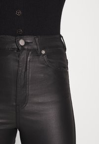 Calças de imitação de couro pretas com cintura alta, fecho de botão, bolsos frontais e uma textura suave e brilhante.