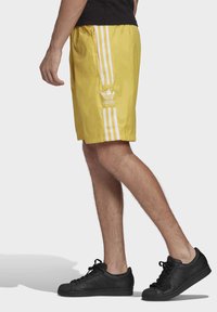 Gula atletiska shorts med vita sidostripes och Adidas-logotyp. Gjorda av lättviktigt tyg, med resår i midjan och hennficka.