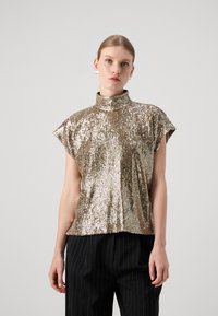 Top senza maniche in oro metallico con colletto alto, caratterizzato da un design a paillettes testurizzate. Abbinato a pantaloni neri con righe sottili.