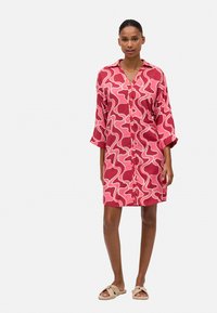 Vestido de camisa de manga corta, abotonado, en rosa con patrones ondulados blancos, fabricado en una tela ligera, con un corte relajado y cuello clásico.