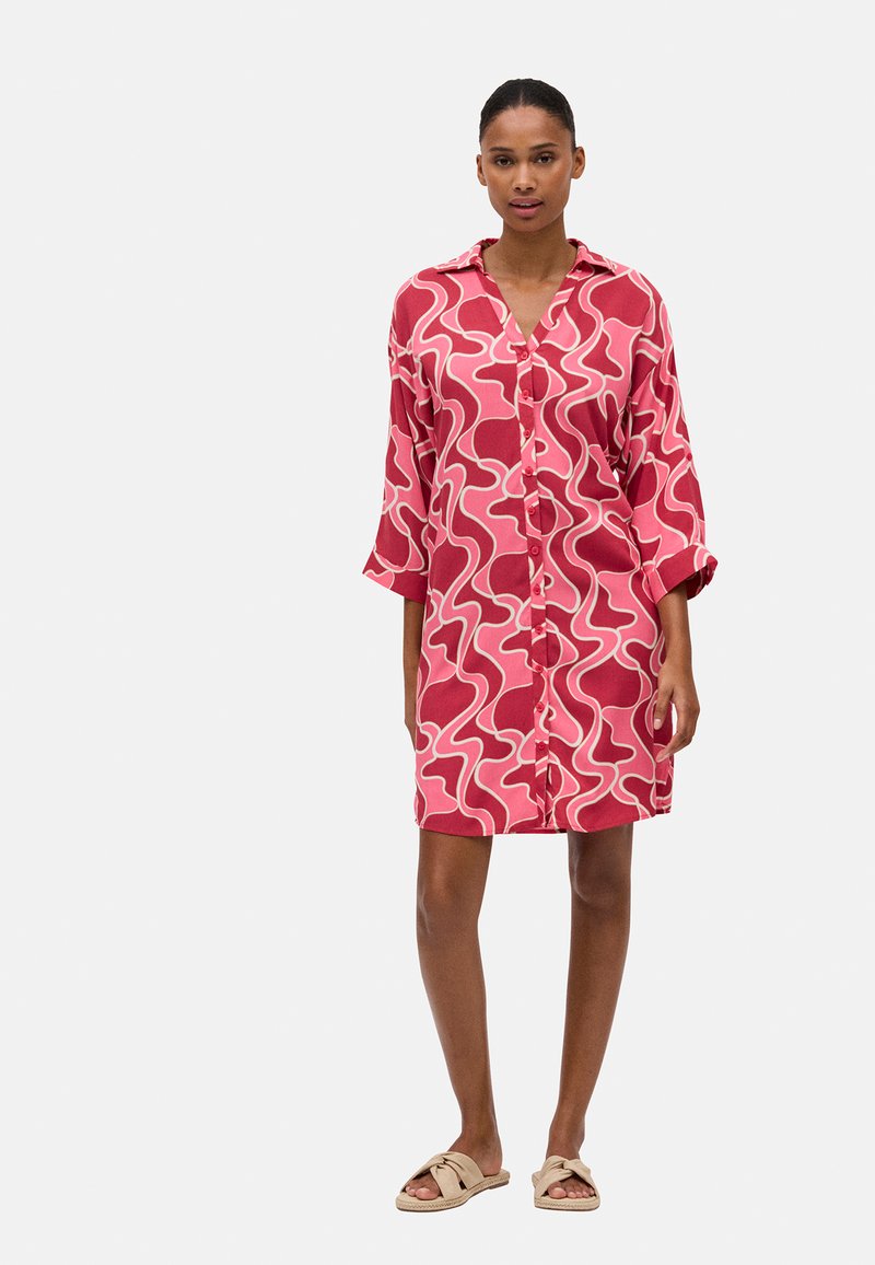 Vestido de camisa de manga corta, abotonado, en rosa con patrones ondulados blancos, fabricado en una tela ligera, con un corte relajado y cuello clásico.