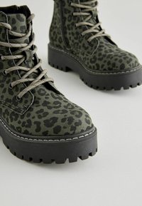 Stivali con stampa leopardata verde, punte tonde, suole nere spesse e lacci grigi. Tessuto texturizzato con dettagli di cucitura a contrasto lungo la suola.