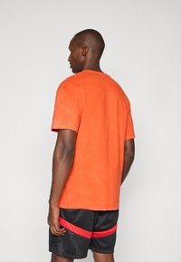Orange bomulds T-shirt med klassisk rund hals, korte ærmer og en let slidt tekstur, parret med sorte mesh shorts med røde striber.