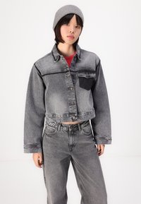 Grå, kort denimjakke med slitt tekstur, knappelukking og brystlomme, parret med vide grå bukser.