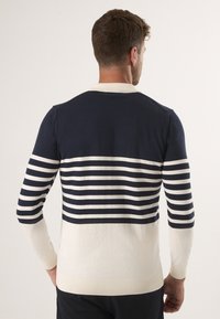 Sweter w pasiastym wzorze w kolorze granatowym i kremowym, charakteryzujący się górną częścią w jednolitym granatowym kolorze oraz poziomymi paskami na rękawach i dolnej części ciała. Ściągacze na mankietach i u dołu.