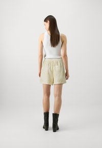 Witte geribbelde tanktop, beige geborduurde shorts met palmenbladontwerpen, elastische tailleband en zwarte hielenkorte laarzen.