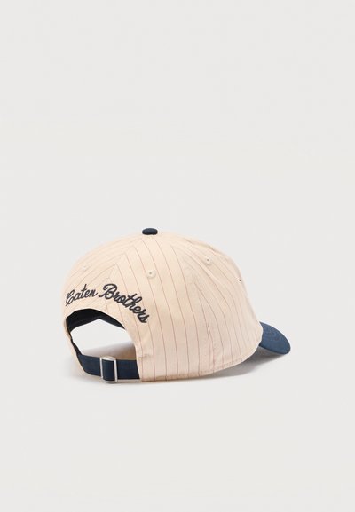 Μπεζ ριγέ καπέλο μπέιζμπολ με σκούρο μπλε γείσο, ρυθμιζόμενο λουράκι και μαύρο κεντημένο κείμενο "Caten Brothers" στο πίσω μέρος.