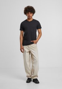 Black short-sleeve t-shirt paired with light beige wide-leg jeans, featuring a relaxed fit and textured fabric. Black sneakers complete the outfit.