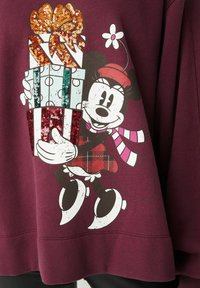 Sweatshirt bordeaux avec un design imprimé d'un personnage de dessin animé tenant des boîtes à cadeaux brillantes et pailletées, ornées d'un nœud rouge et d'une fleur.