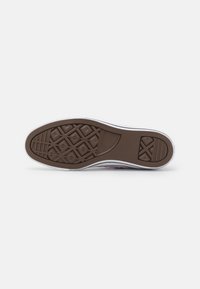 Sola de borracha castanha com padrão de textura, entressola branca e bordas suaves. Calcanhar reforçado e detalhe de marca visíveis.