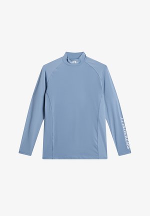 Långärmad ljusblå skjorta av mjukt, stretchigt tyg. Har en hög krage och en vit logotryck på vänster ärm.