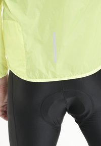 Gul lättviktig jacka med reflekterande remsa, matchad med svarta cykelbyxor som har en vadderad insats för komfort.