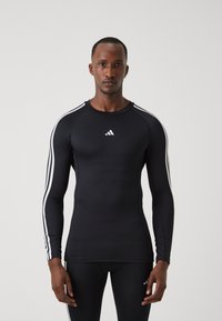 Fekete, hosszú ujjú sportpóló feh�ér Adidas logóval és három fehér csíkkal az ujjak mentén. Feszes, texturált anyagból készült.