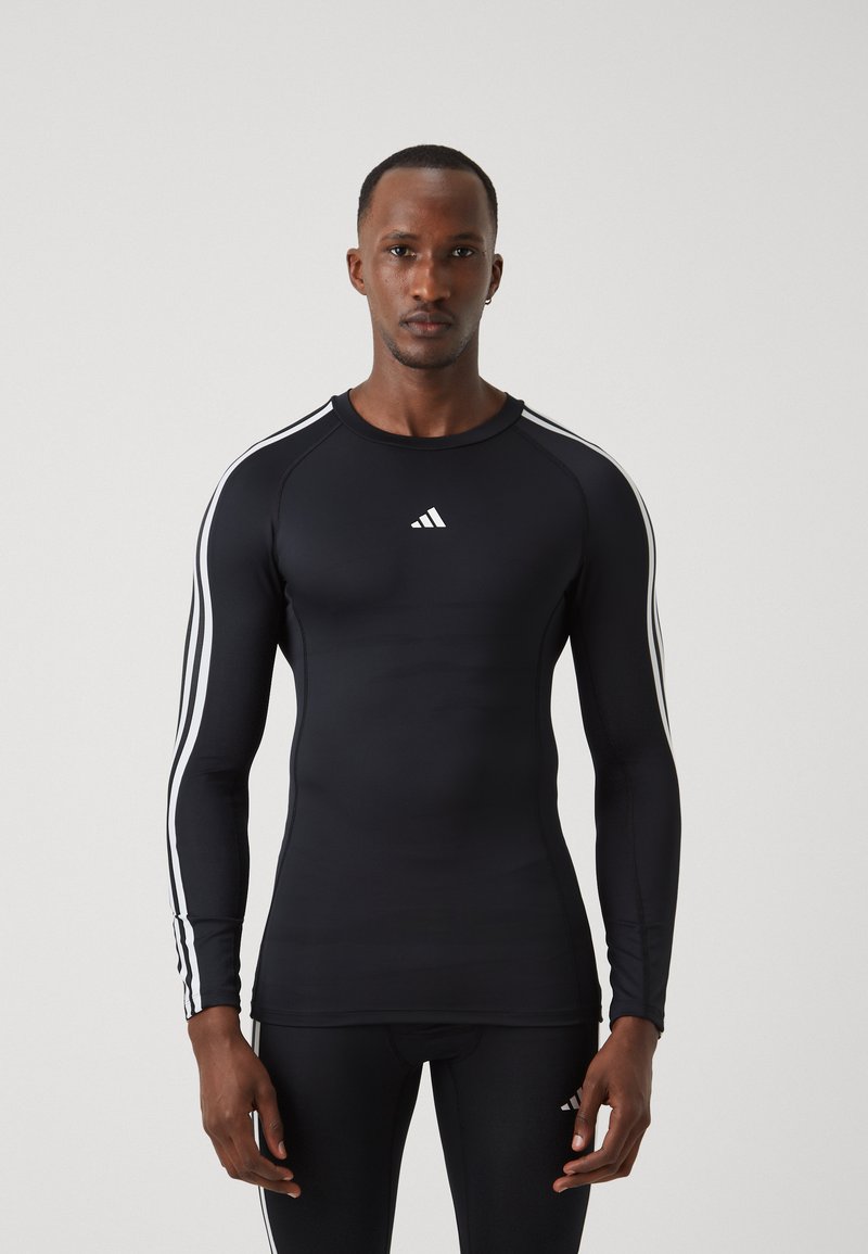 Fekete, hosszú ujjú sportpóló fehér Adidas logóval és három fehér csíkkal az ujjak mentén. Feszes, texturált anyagból készült.
