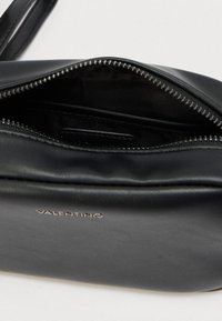 Μαύρη δερμάτινη τσάντα χειρός με φερμουάρ, που παρουσιάζει ομαλή υφή και εσωτερική επένδυση από ύφασμα. Διαθέτει ανάγλυφο λογότυπο.